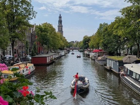 Un canale di Amsterdam con le case galleggianti e una barca che passa